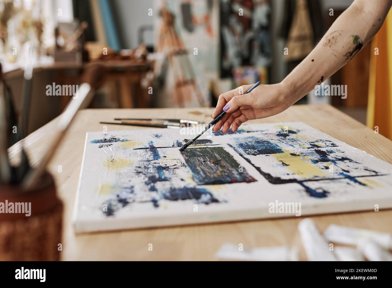 Mano di giovane craftwoman che tiene il pennello sopra la tela mentre crea il nuovo capolavoro a piacere o durante la lezione di pittura in studio Foto Stock