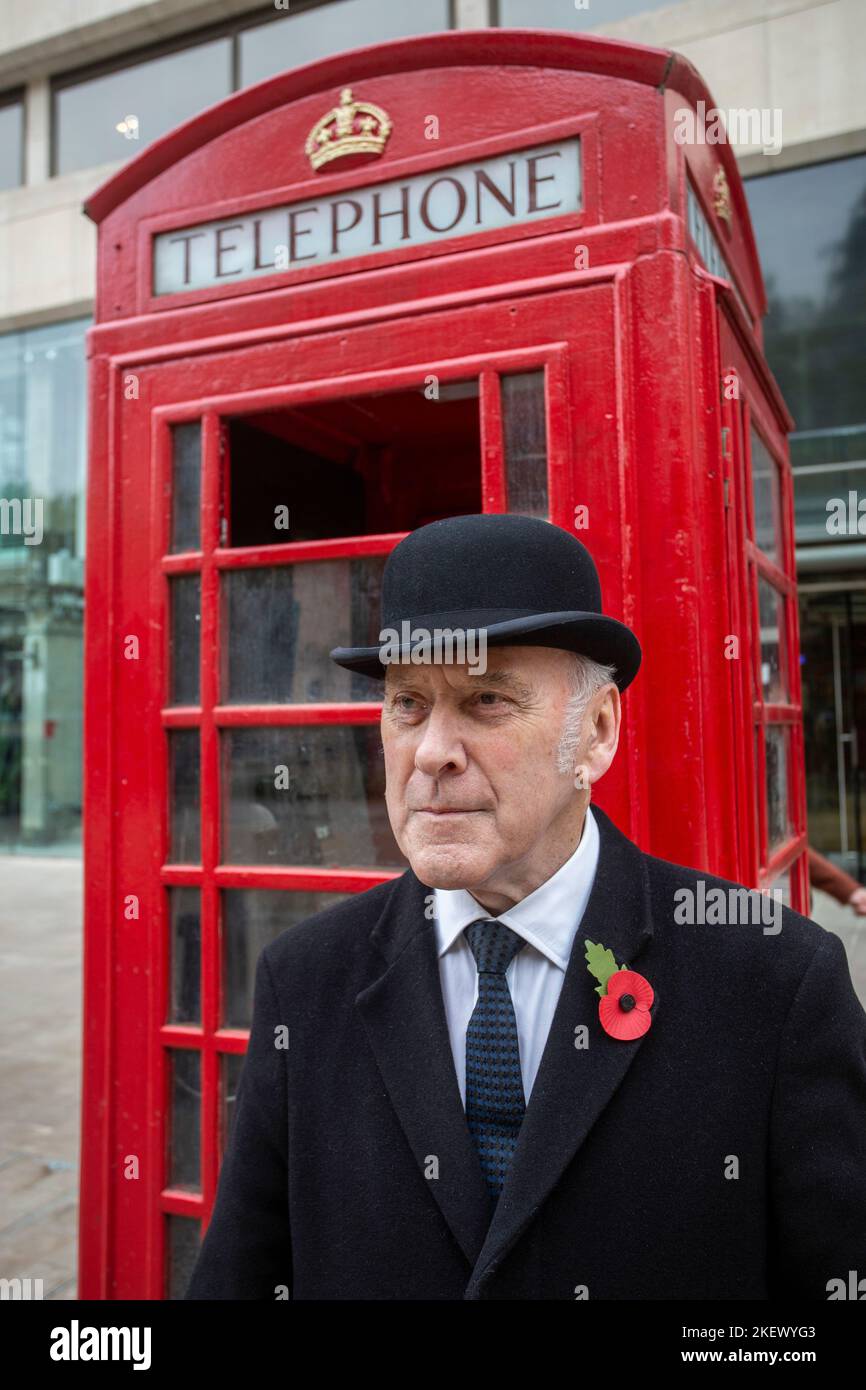 gentleman inglese in cappello di boccaio di fronte alla tradizionale scatola telefonica rossa britannica Foto Stock