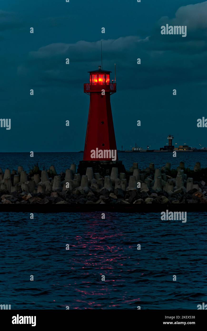 Cartolina dal mare con un faro la sera. Sono visibili i riflessi di luce del faro sulla superficie del mare. Foto Stock