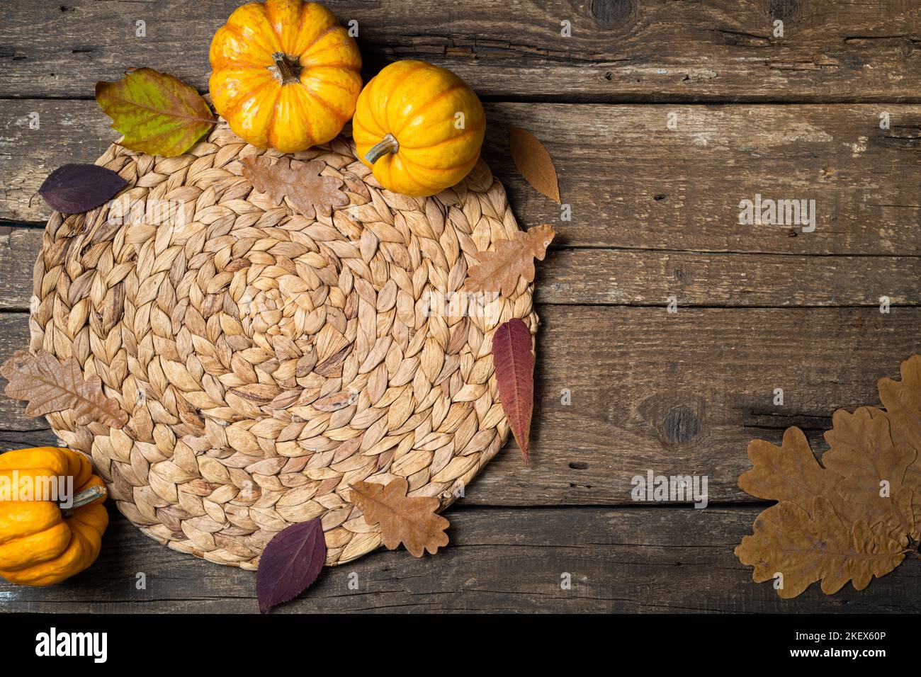 Accogliente tavolo da hygge. Vista dall'alto del tappetino in vimini, zucche, foglie autunnali, candela su tavolo scuro. Tabella di autunno impostazione. Sfondo festivo del Ringraziamento. Foto Stock