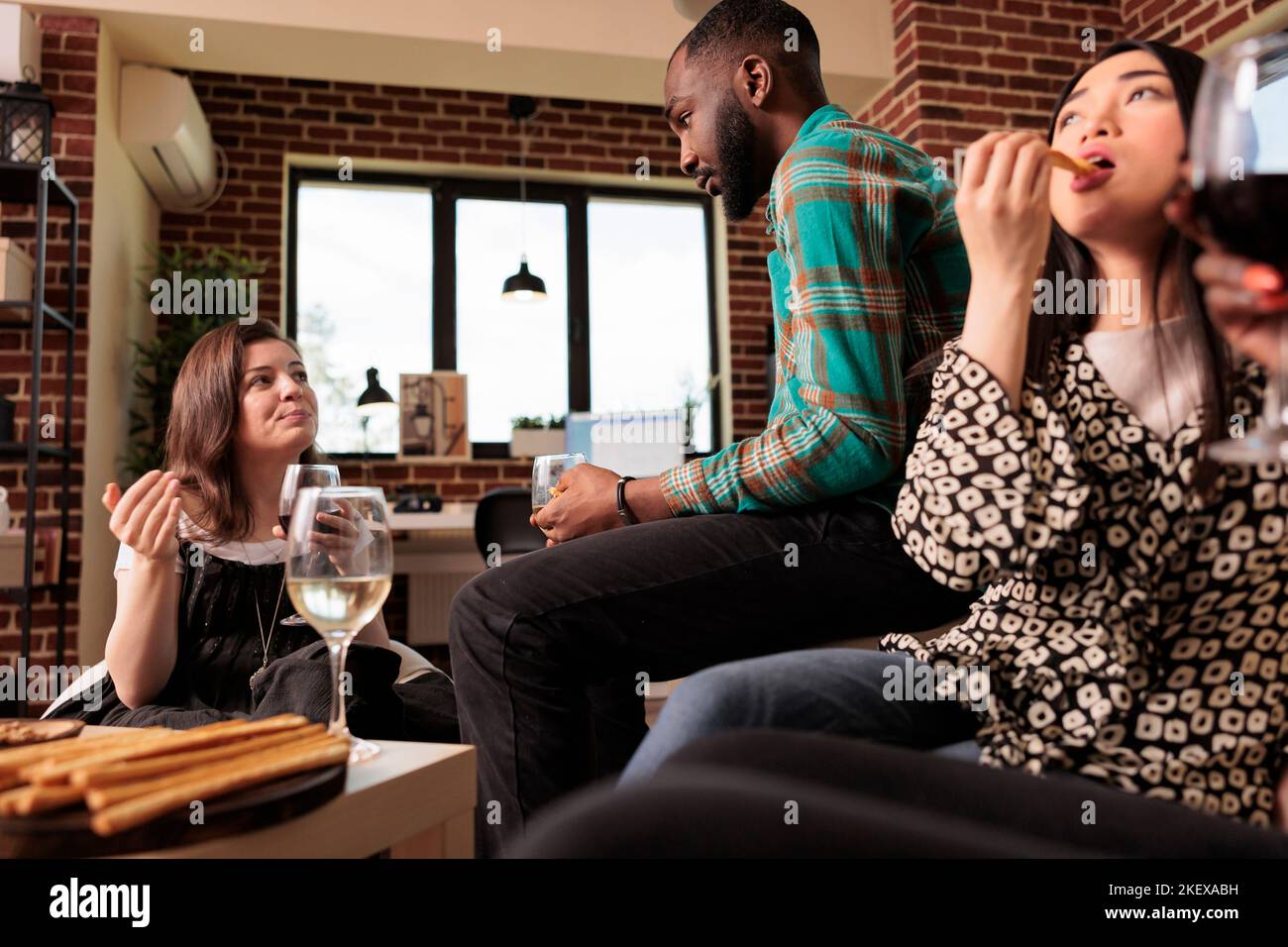 afroamericano adulto maschio ascoltare, ascoltare attentamente donna caucasica parlare, conversazione, discussione, argomento a appartamento partito. Asian mangiare bastoni di pane, bere vino, concentrarsi. Foto Stock