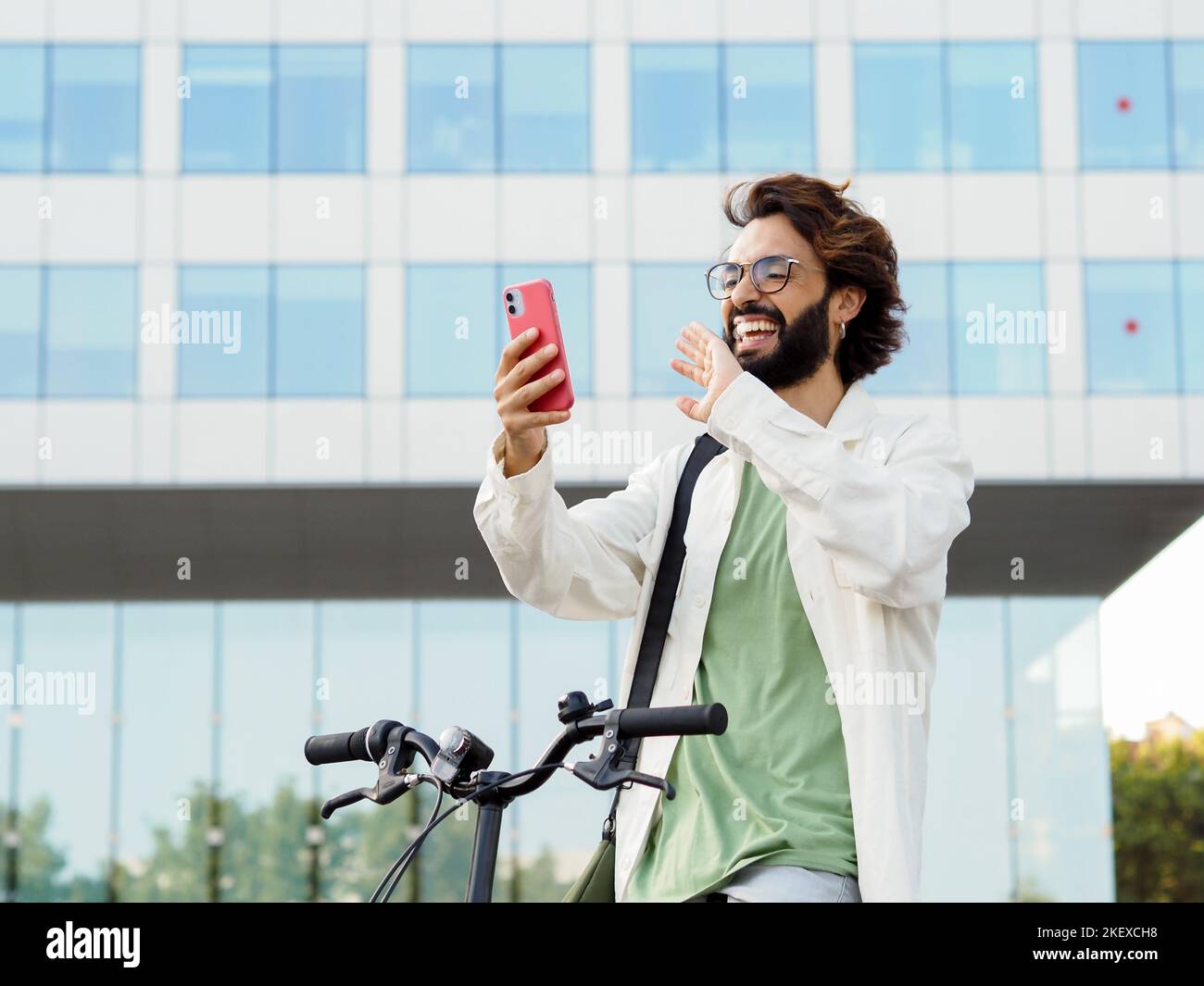 Giovane uomo d'affari italiano con una bicicletta che effettua una videochiamata con uno smartphone. Giovane uomo intraprendente Foto Stock