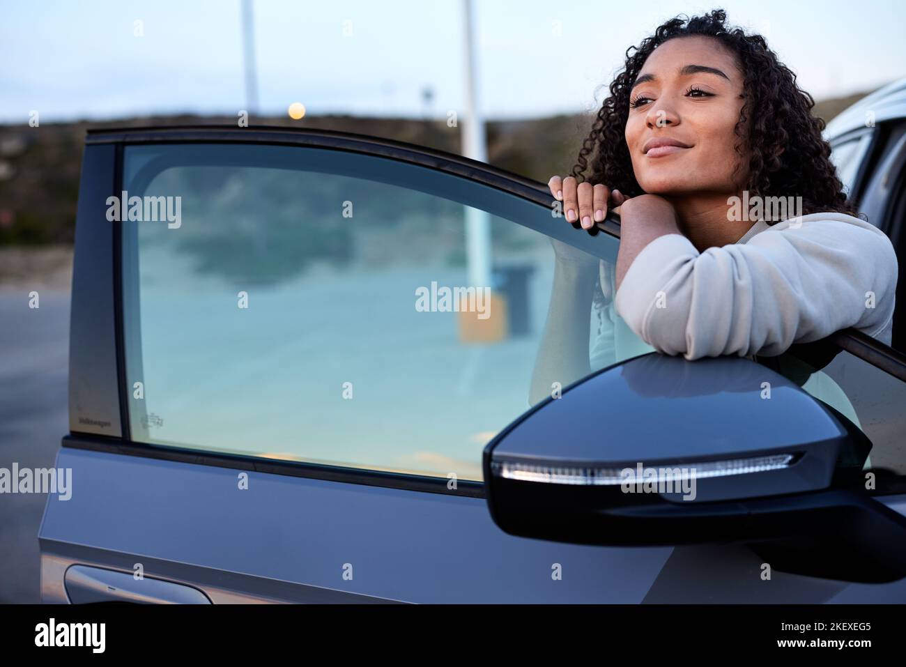Donna sorridente giorno sognando mentre si appoggia sulla porta del veicolo Foto Stock