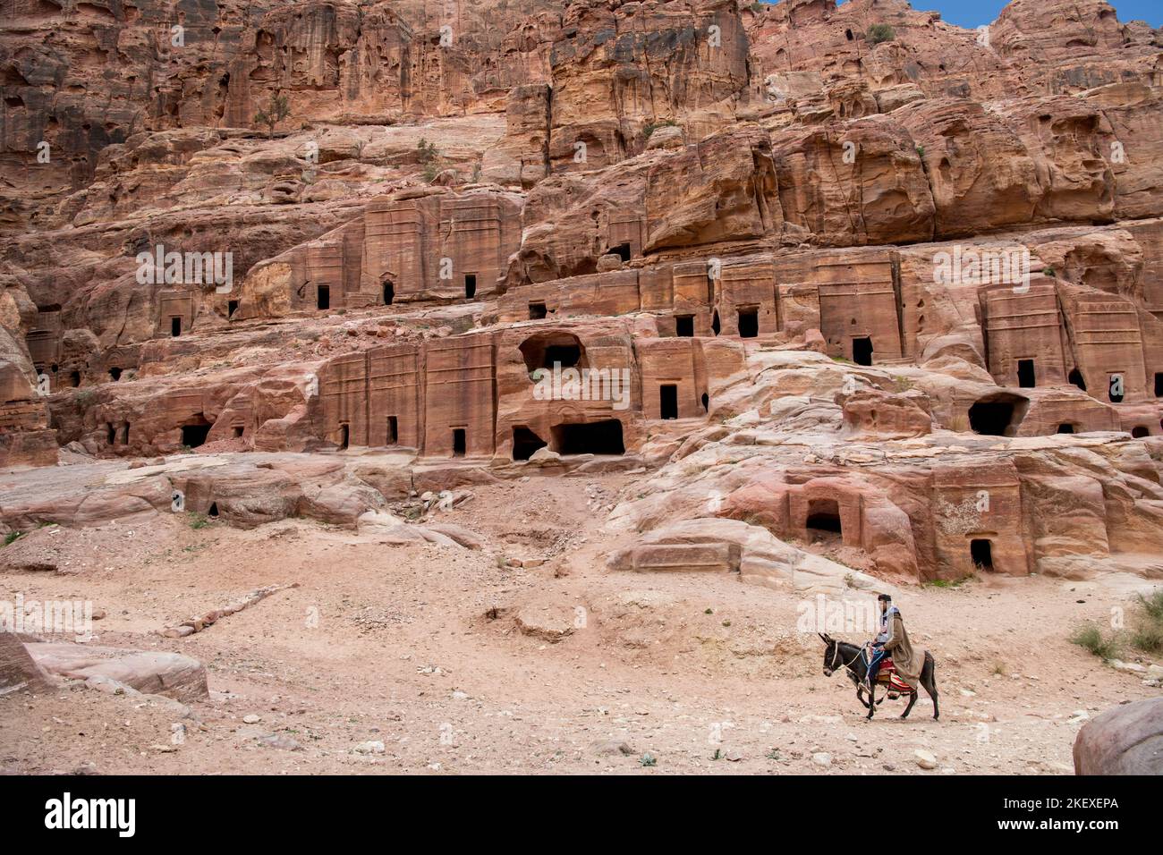 Uomo in sella asino passato tombe Nabataean Petra Jordan Foto Stock