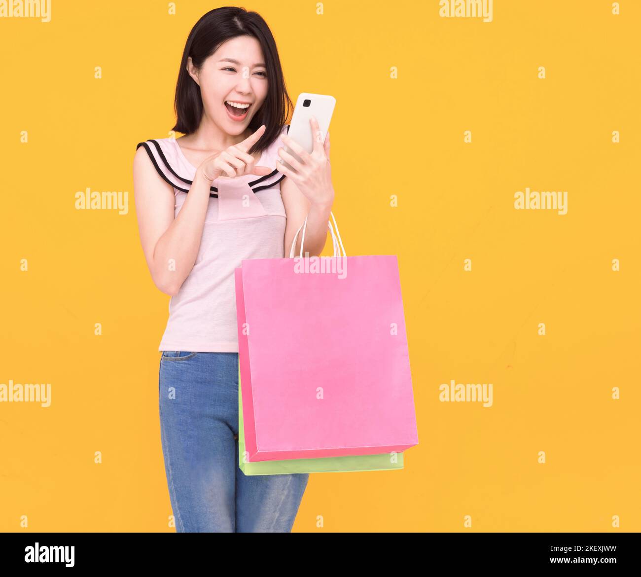 Felice giovane donna guardando il telefono cellulare e tenendo borse per la spesa Foto Stock