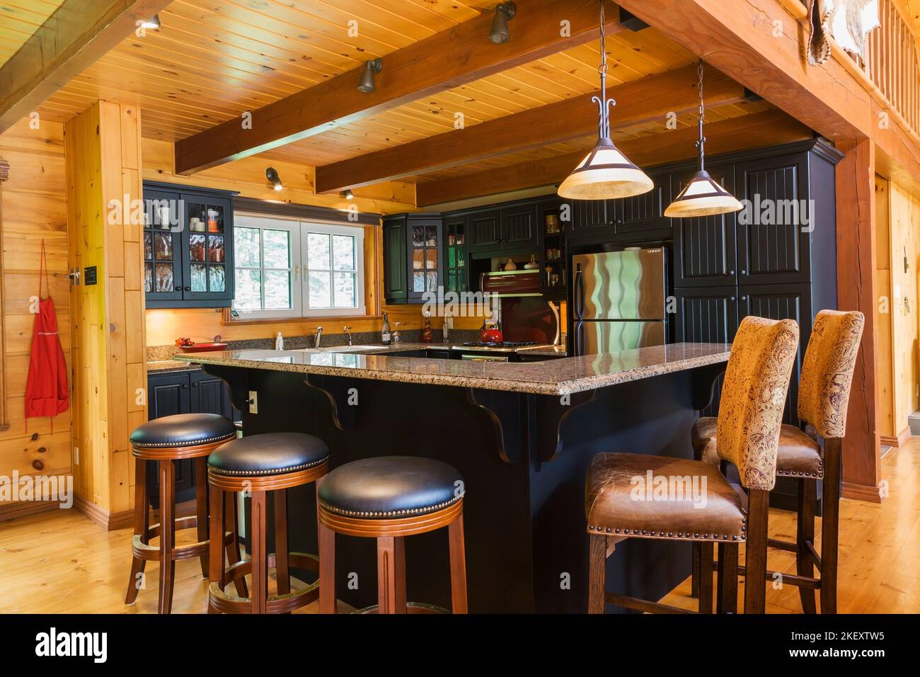Cucina con armadietti di legno nero, isola con granito countertop e pelle imbottita sgabelli barstole all'interno di un cottage fresato stile piatto profilo di tronchi casa. Foto Stock