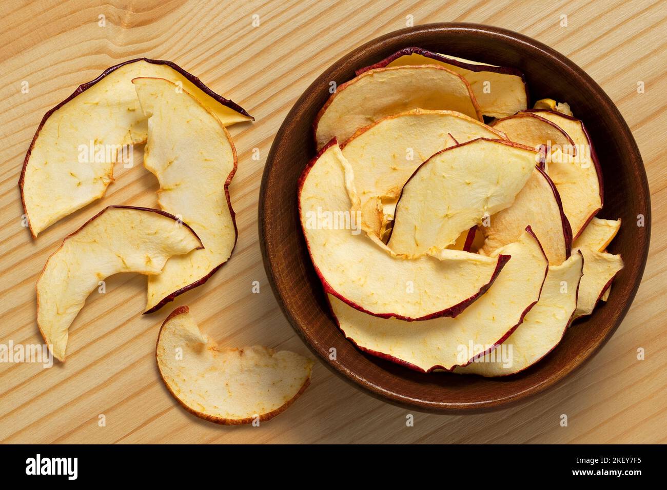 Fette di mela essiccate in una ciotola di legno marrone accanto alle fette di mela essiccate versate su fondo di legno chiaro. Vista dall'alto. Foto Stock