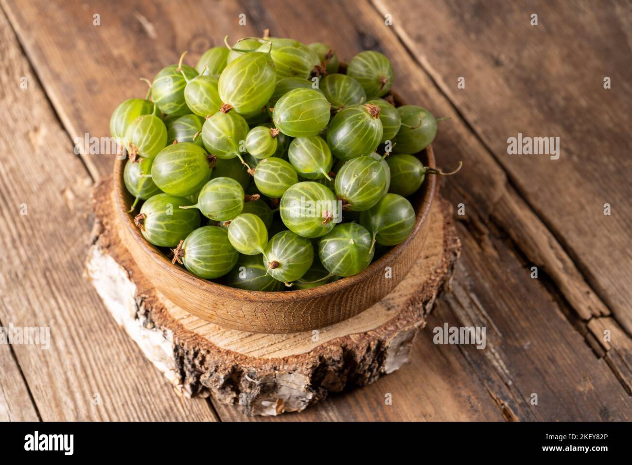 Frutti di bosco verdi in una ciotola di legno. Raccogliere bacche su un tavolo di legno. Cibo vitaminico estivo di uva spina. Foto Stock