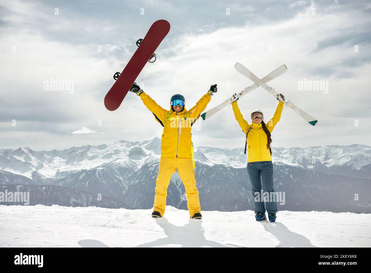 Un paio di sciatori e snowboarder sono in piedi in cima alla montagna, tenendo in mano sci e snowboard e divertendosi. Sport invernali presso la stazione sciistica Concept Foto Stock