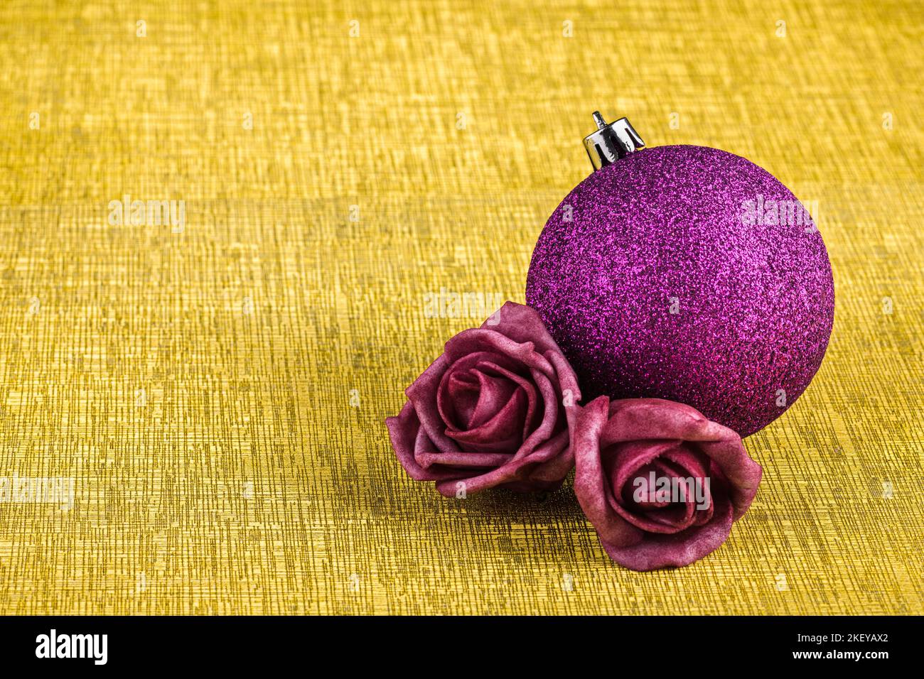 Un baule di natale viola con glitter e due rose in feltro isolato su uno sfondo dorato con texture. Foto Stock