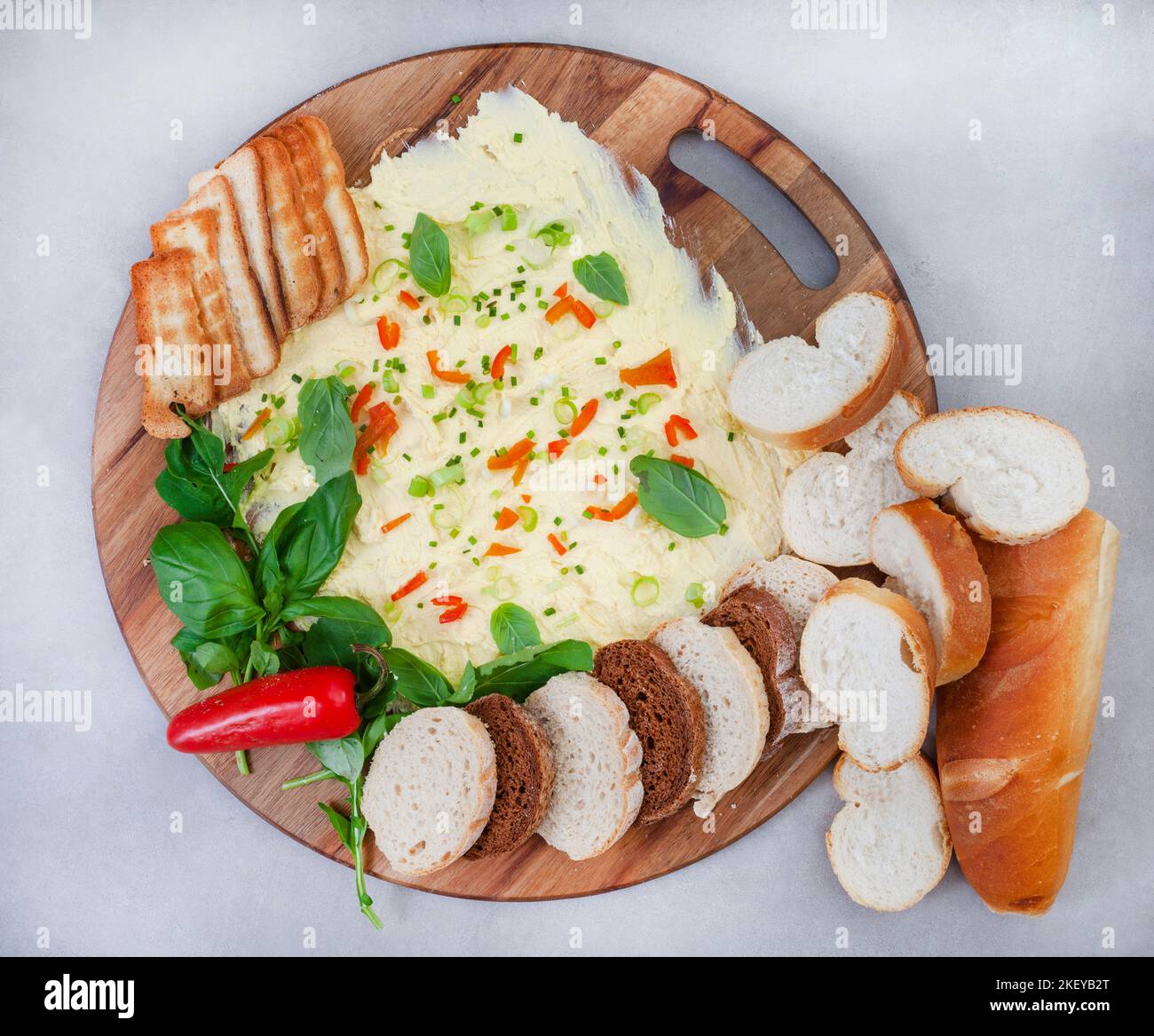 Butter board, il nuovo modo alla moda per servire il pane e gli antipasti. Burro con jalapeno, cipollina, erba cipollina e altre erbe, servito con selezione o Foto Stock