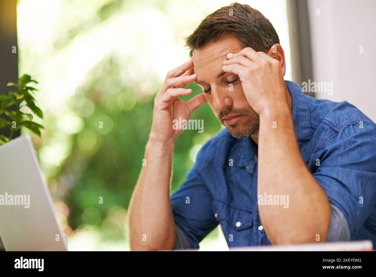 Lo stress gli sta arrivando, un uomo che soffre di mal di testa mentre lavora da casa. Foto Stock
