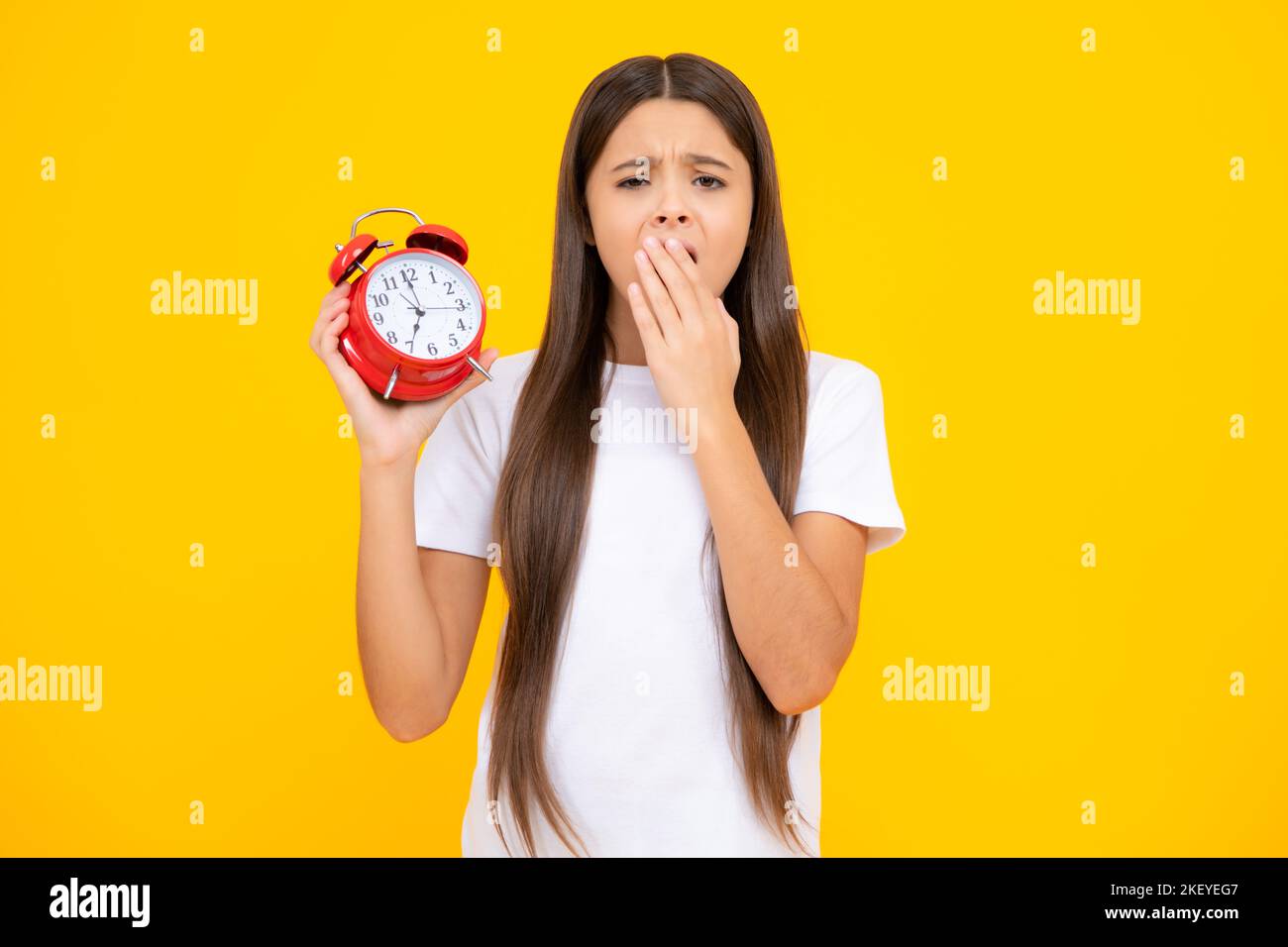 Ragazza adolescente stanca e annoiato. Bambino che tiene l'orologio su sfondo giallo. Mattina presto, programma quotidiano. Check-in bambini. Non essere in ritardo Foto Stock