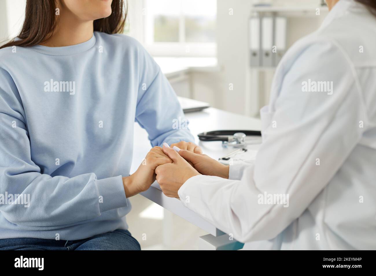 La dottoressa tiene la mano della paziente femminile, confortandola, esprimendo simpatia e sostegno. Foto Stock
