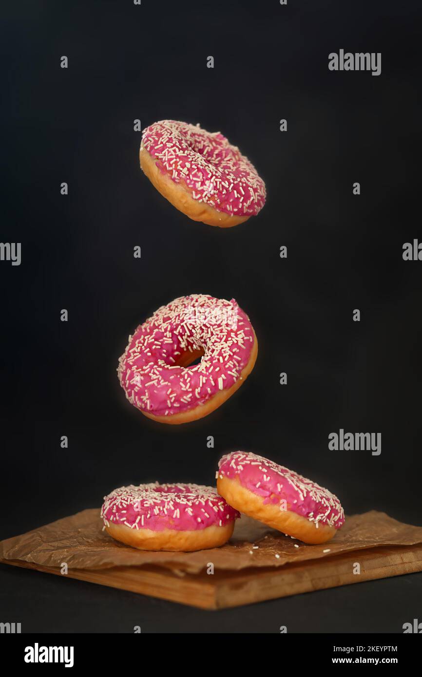 Mini ciambelle fatte in casa smaltate che si levitano nello spazio su uno sfondo nero Foto Stock