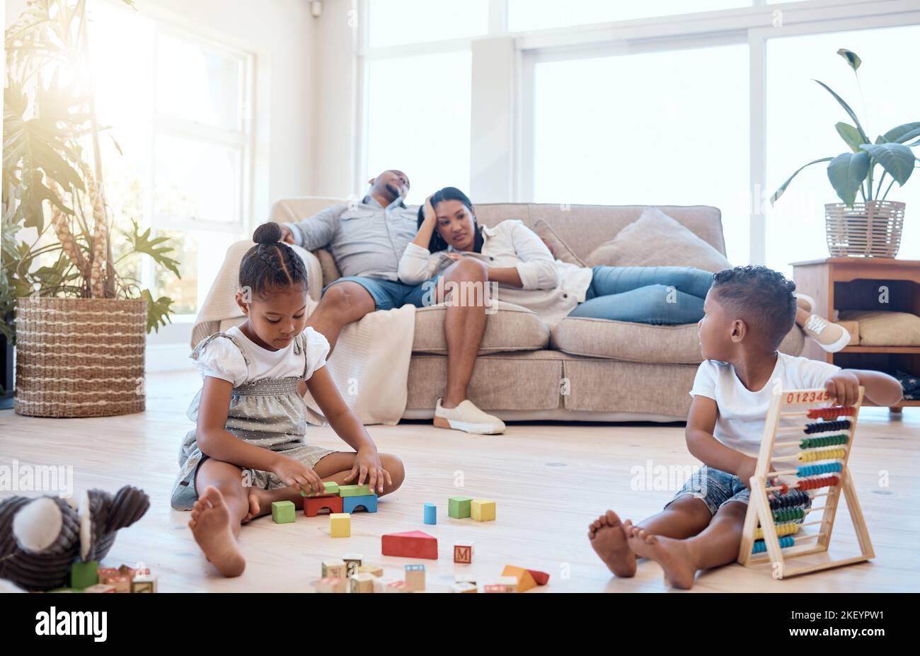 Genitori stanchi sul divano, bambini e giocare con i giocattoli nel fine settimana per rilassarsi, per il legame e sonnolenza in salotto. Famiglia, madre e padre con fratello Foto Stock