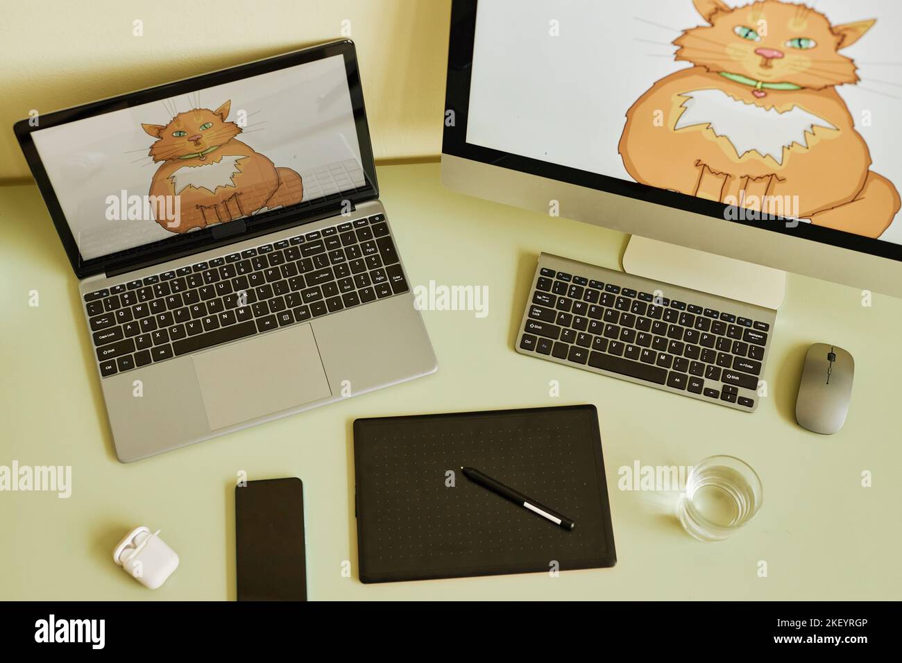 Vista dall'alto di laptop e computer con gatto rosso grasso sugli schermi sul posto di lavoro di artista digitale con dispositivi mobili e desktop Foto Stock