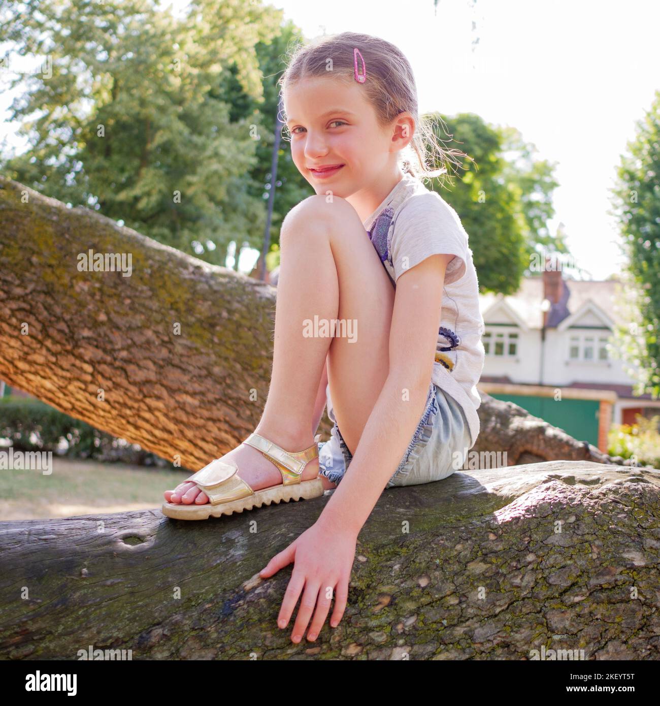 Ritratto di una giovane ragazza felice di otto anni seduta su un ramo d'albero nel parco, Inghilterra, Regno Unito Foto Stock