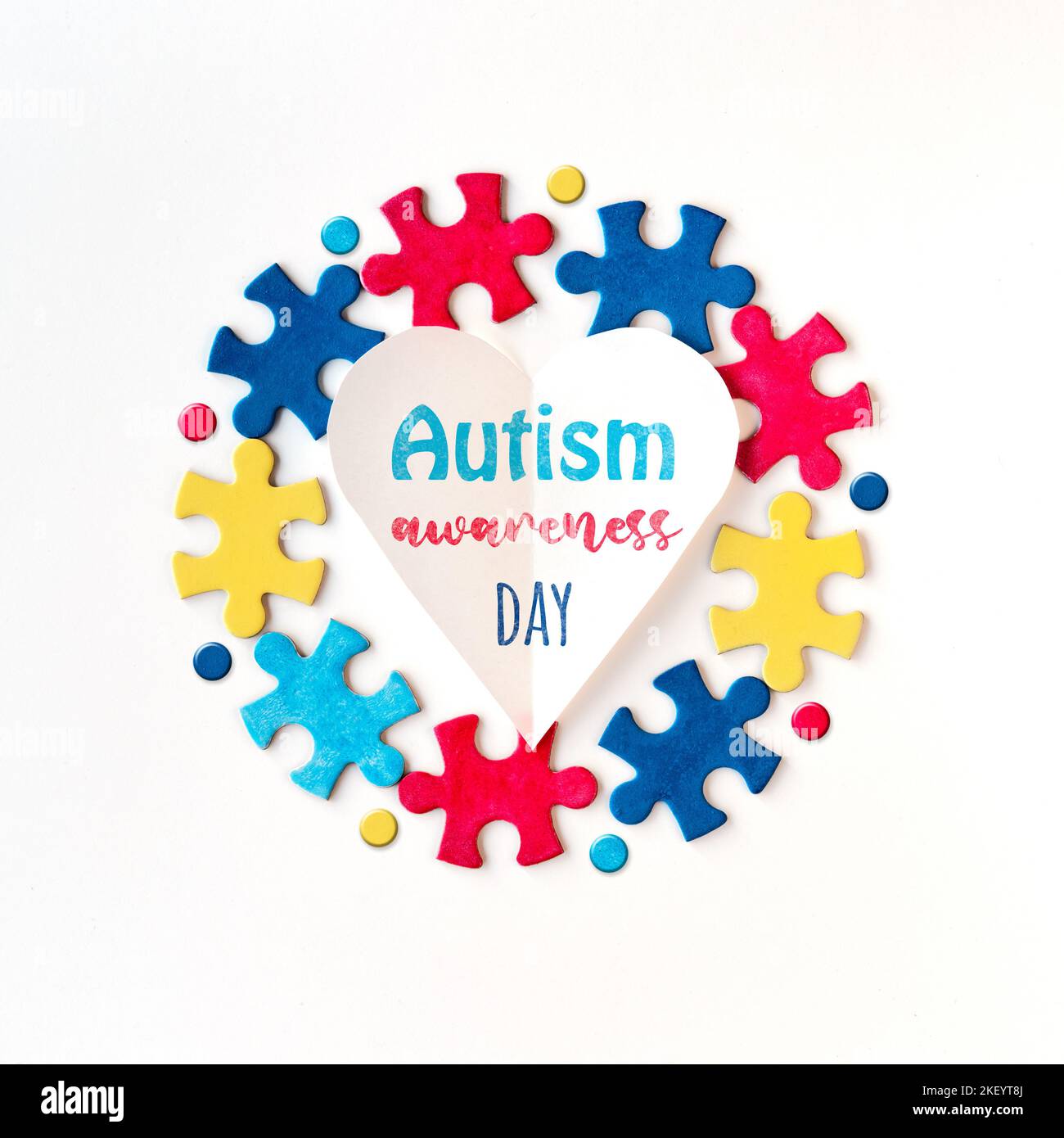 Simboli della campagna autismo. Pezzi di puzzle intorno al cuore di carta con parola Autism consapevolezza giorno. Disposizione piatta, vista dall'alto, composizione quadrata. Foto Stock