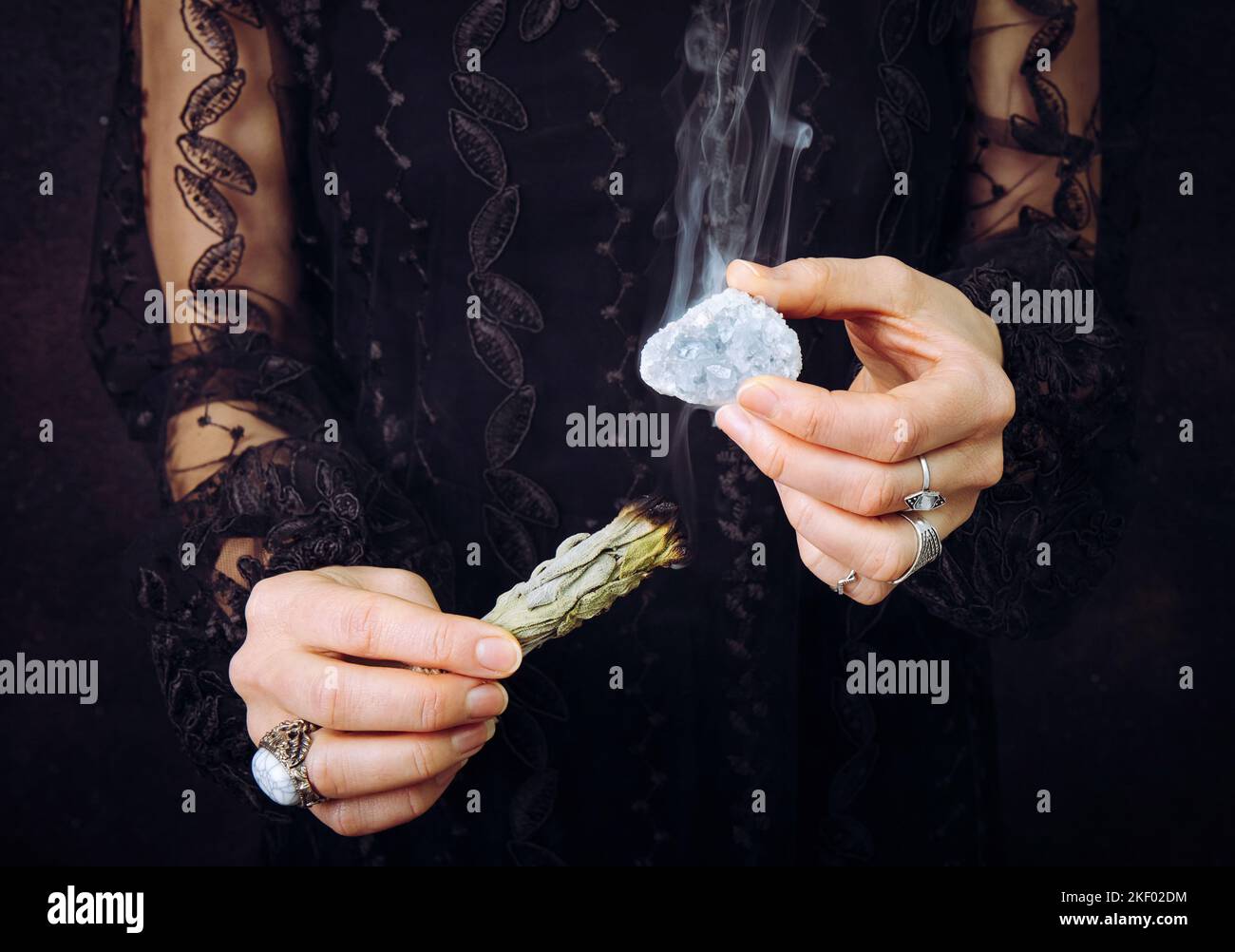 Vista ravvicinata della donna in abito di pizzo nero, gemma di cristallo celeste di pulizia macchiando il fascio di salvia bianco. Rimuovere l'energia negativa. Foto Stock