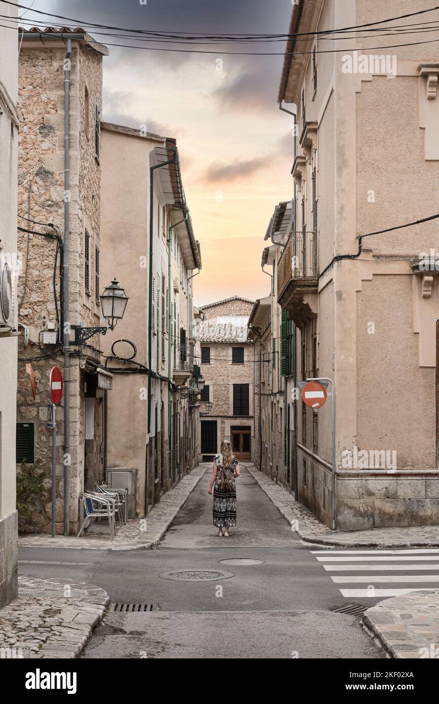 Vista posteriore della donna in vestito lungo in piedi nel mezzo di strada stretta tra case storiche nella città vecchia spagnola di Soller Foto Stock