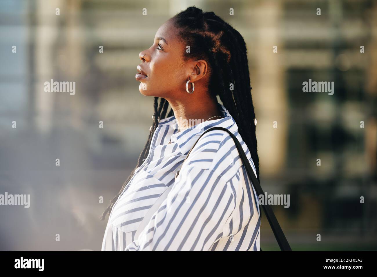 Vista laterale di una giovane donna d'affari che guarda premurosa mentre si trova all'aperto in città. Giovane donna d'affari nera che si trova al lavoro al mattino. Foto Stock