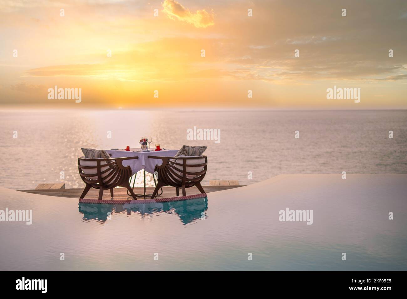 Vista sul mare sotto la luce del tramonto con tavolo da pranzo con piscina a sfioro intorno. Fuga tropicale romantica per due, concetto di coppia. Sedie, cibo romantico Foto Stock