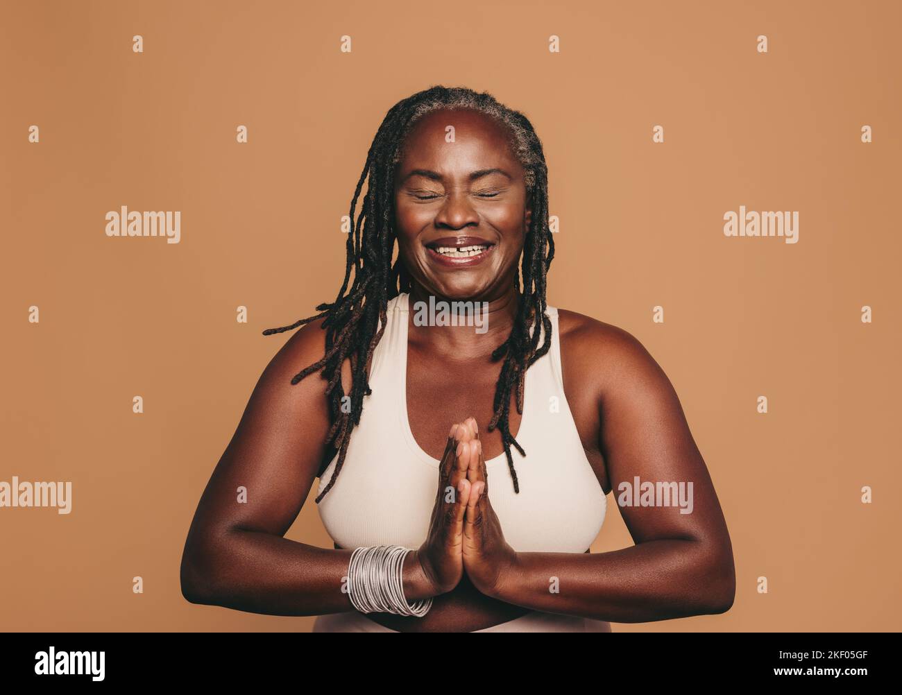 Donna felice che medita con gli occhi chiusi e le mani in posizione di preghiera. Donna sorridente con greggi che praticano lo yoga in uno studio. Sportivo maturo Foto Stock