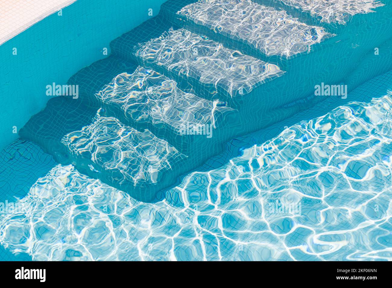 Primo piano dei gradini della piscina e dell'acqua blu limpida. L'entrata della piscina nuova e moderna è a pochi passi con acqua pulita e fresca e rinfrescante su un caldo luminoso Foto Stock