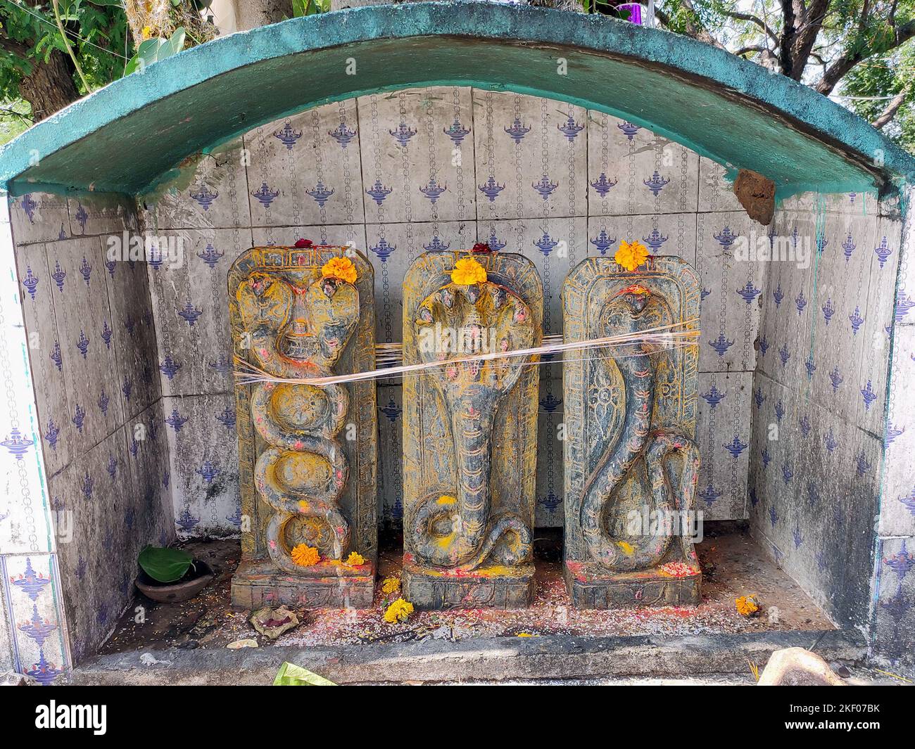 Un santuario sereno dedicato a Nagas, o divinità serpenti, è catturato in questa immagine. Tre sculture in pietra intagliate di Nagas. Foto Stock