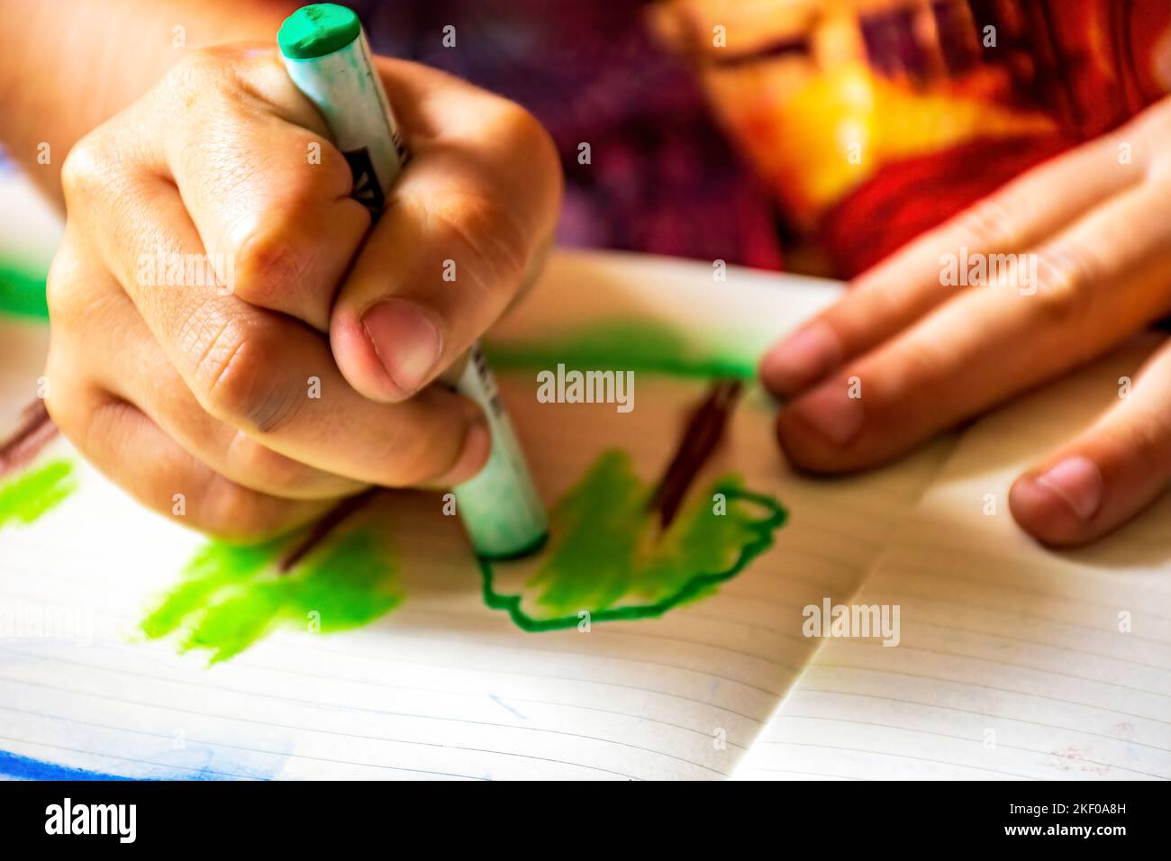 Disegno delle mani del bambino con pastello su un foglio di carta illuminato dalla luce laterale dalla finestra Foto Stock