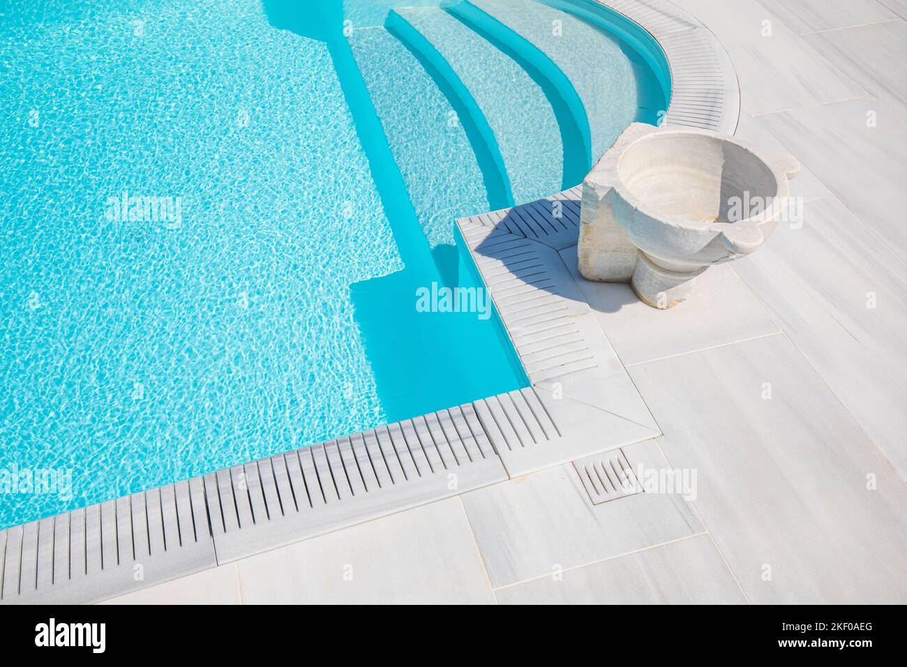 Piscina con scale ed eleganti gradini in pietra a forma di navata in acqua azzurra. Piscina di lusso con vaso in marmo durante il sole. Estate all'aperto spa Foto Stock