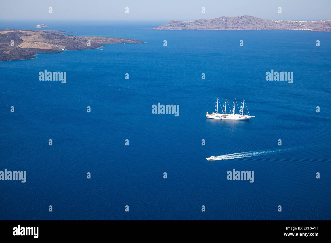 Nave da crociera sul mare blu profondo dell'isola di Santorini, nella baia della Grecia con piccole barche da trasporto. Vacanze estive, tour turismo persone nel Mediterraneo Foto Stock