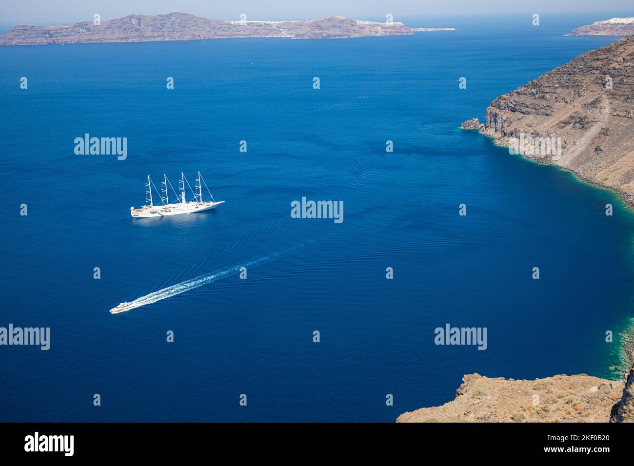 Nave da crociera sul mare blu profondo dell'isola di Santorini, nella baia della Grecia con piccole barche da trasporto. Vacanze estive, tour turismo persone nel Mediterraneo Foto Stock
