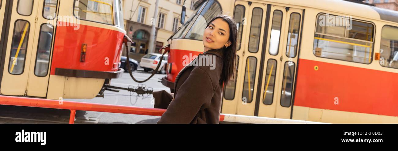 Donna elegante in cappotto in piedi vicino al tram in strada urbana a Praga, banner, immagine stock Foto Stock