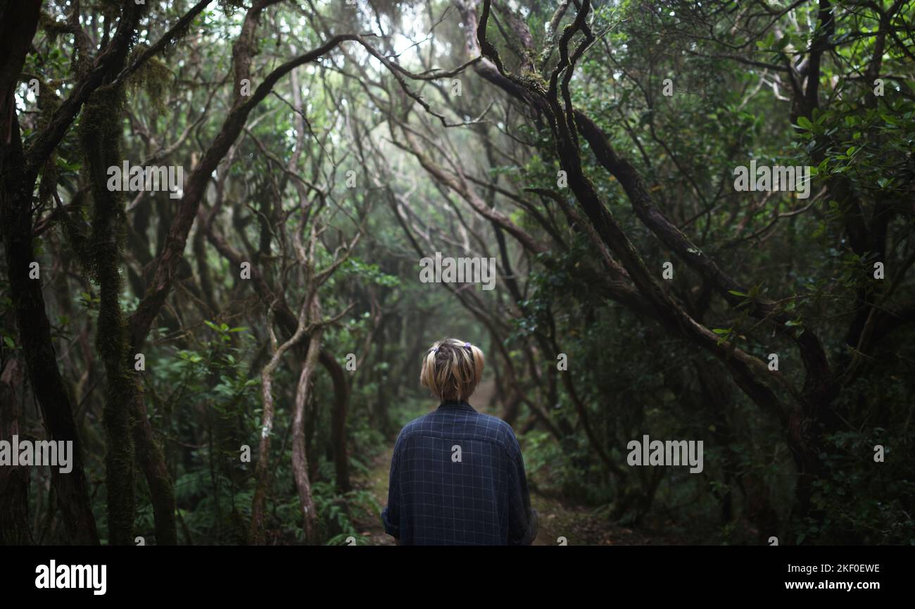 Una giovane donna con capelli corti in piedi su un sentiero in una foresta scura di alberi ritorti Foto Stock