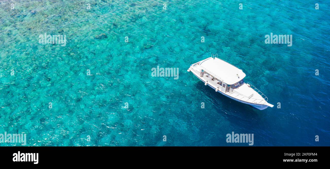 Piccolo yacht di lusso che si aggrappa in acque poco profonde. Vista aerea di isola tropicale spiaggia vacanza yacht sulla barriera corallina blu oceano, sport all'aperto, attività estive Foto Stock