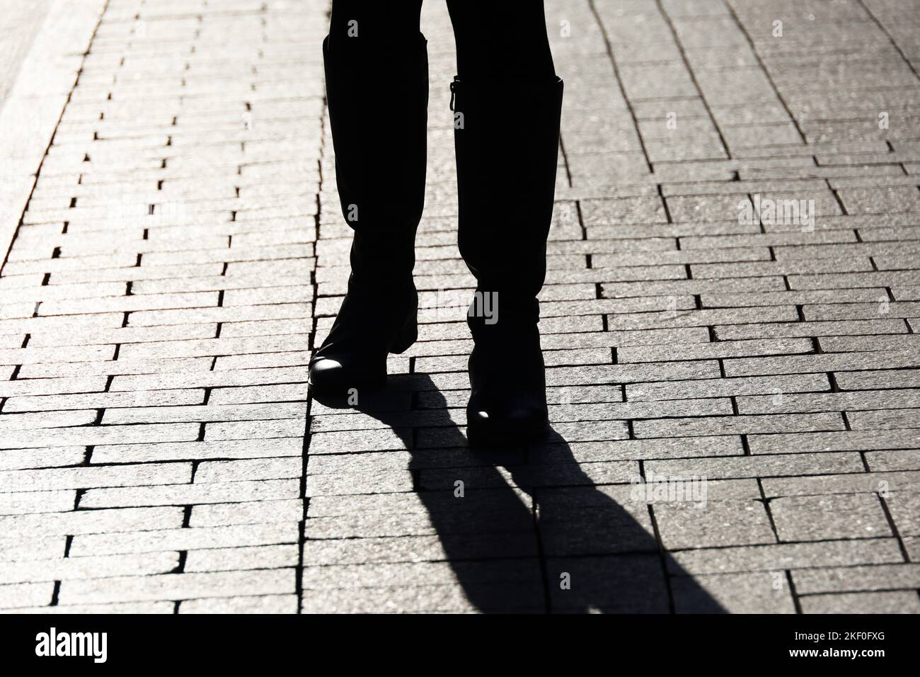 Gambe femminili in stivali su una strada, silhouette nera e ombra di donna che cammina sul marciapiede pavimentato Foto Stock