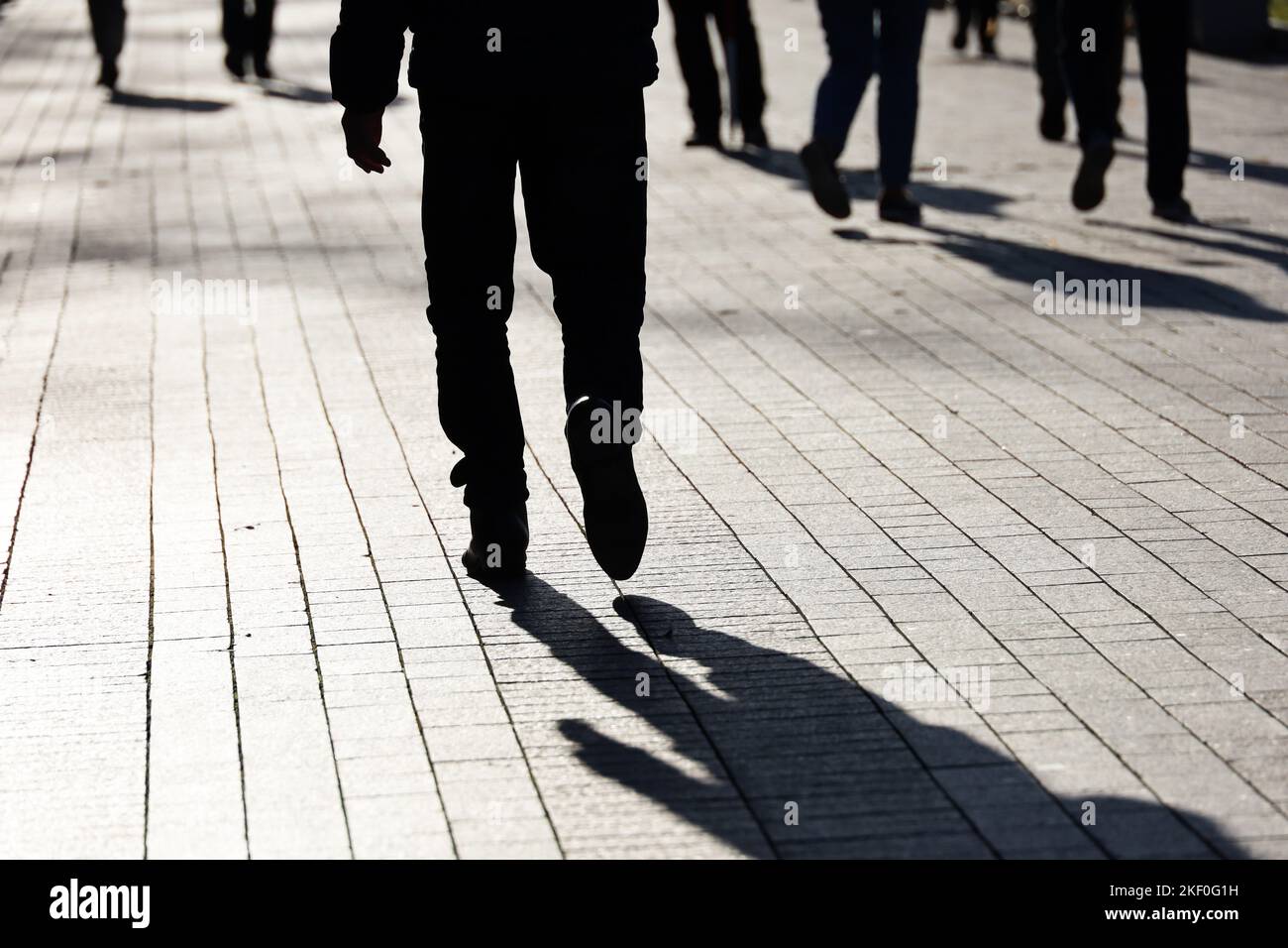 Silhouette nera e ombra dell'uomo che cammina su una strada. Gambe maschili sulla folla di persone sfondo, la vita cittadina Foto Stock
