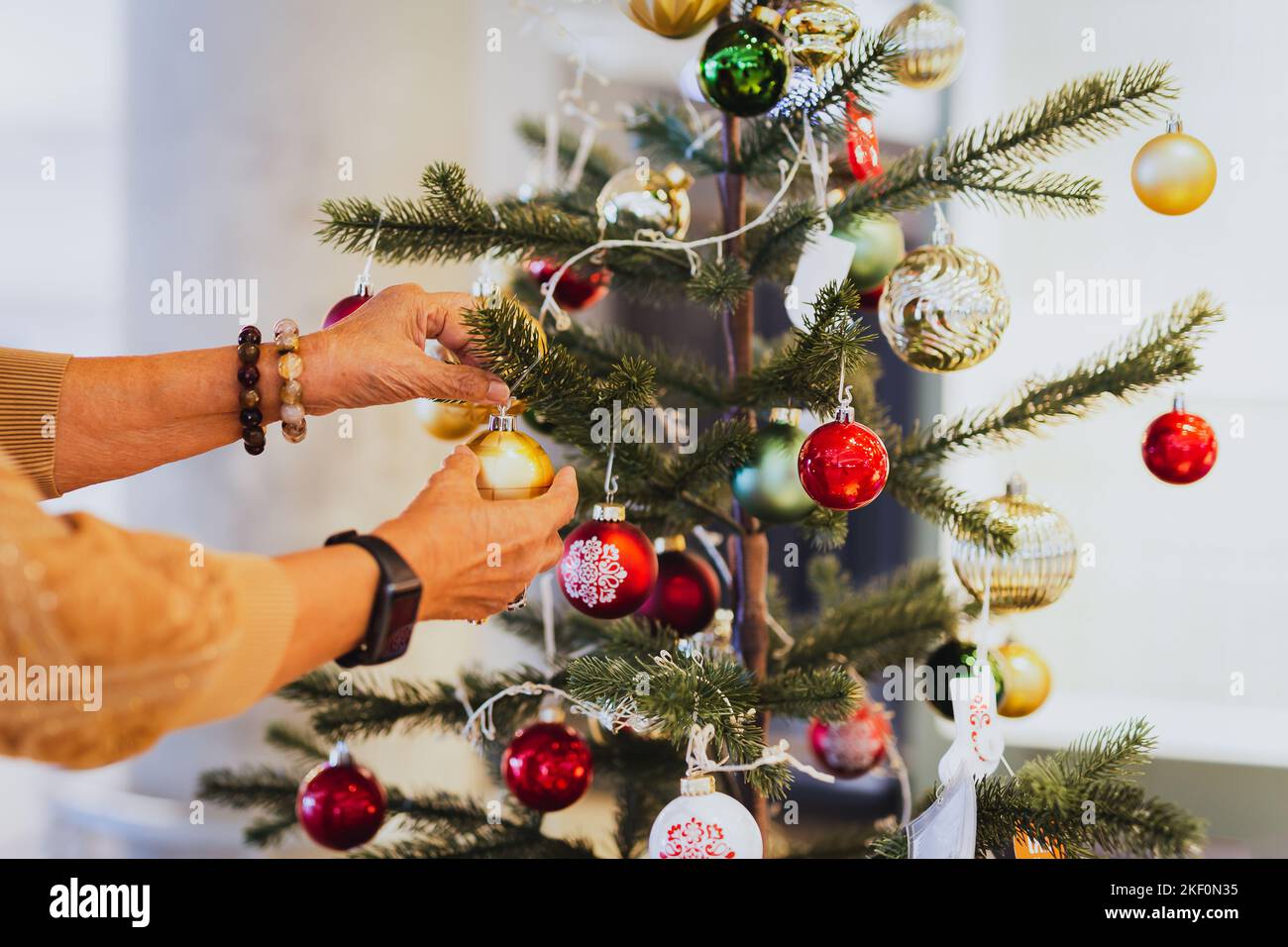 Donna anziana che decora un albero di Natale a casa. Foto Stock