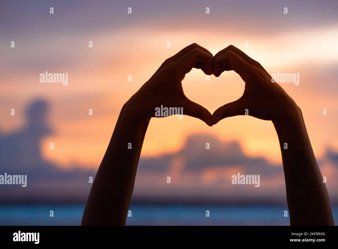 Le mani formano un cuore con la silhouette del tramonto Foto Stock