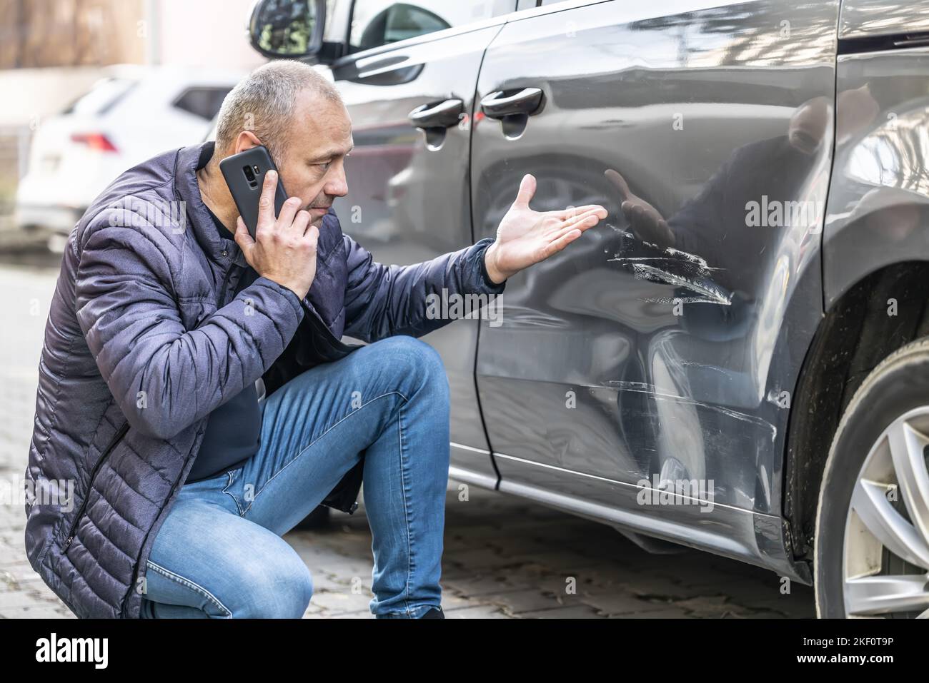 Un uomo chiama la compagnia di assicurazione a causa della porta danneggiata della sua auto perché il colpevole dell'incidente è scappato dal parcheggio. Foto Stock