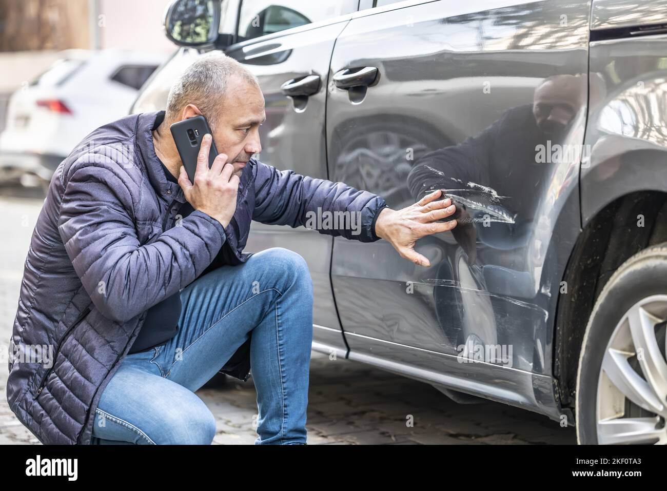 Un uomo chiama la compagnia di assicurazione o la polizia perché qualcuno ha appoggiato nella porta laterale della sua auto nel parcheggio. Foto Stock