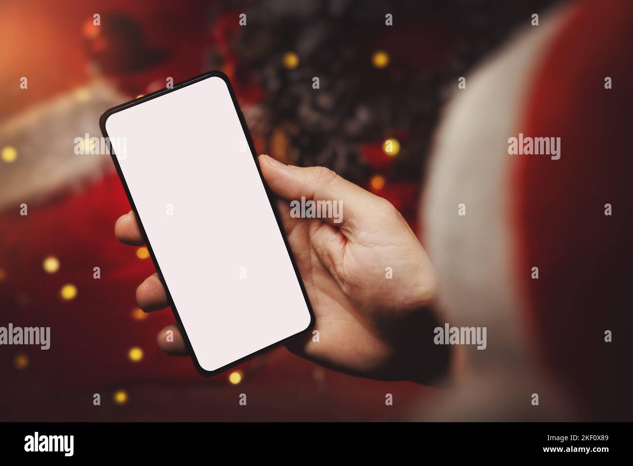 uomo con cappello di santa che tiene il telefono cellulare in mano con schermo bianco su sfondo decorazioni di natale. shopping regalo online e pubblicità Foto Stock