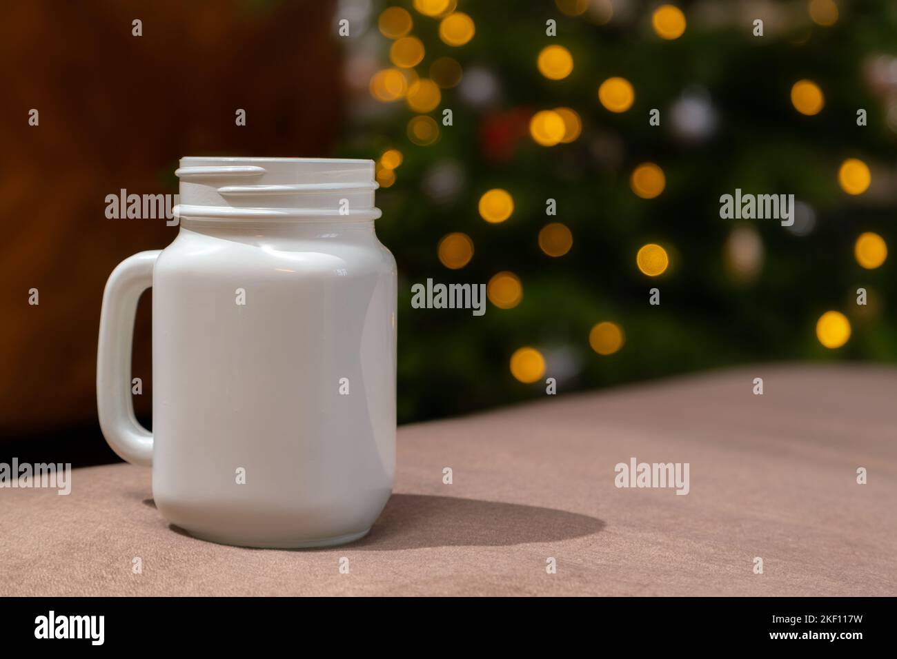Coppa bianca di natale che si posa sul tavolo. Luci sfocate sullo sfondo della tazza di Natale. Foto Stock