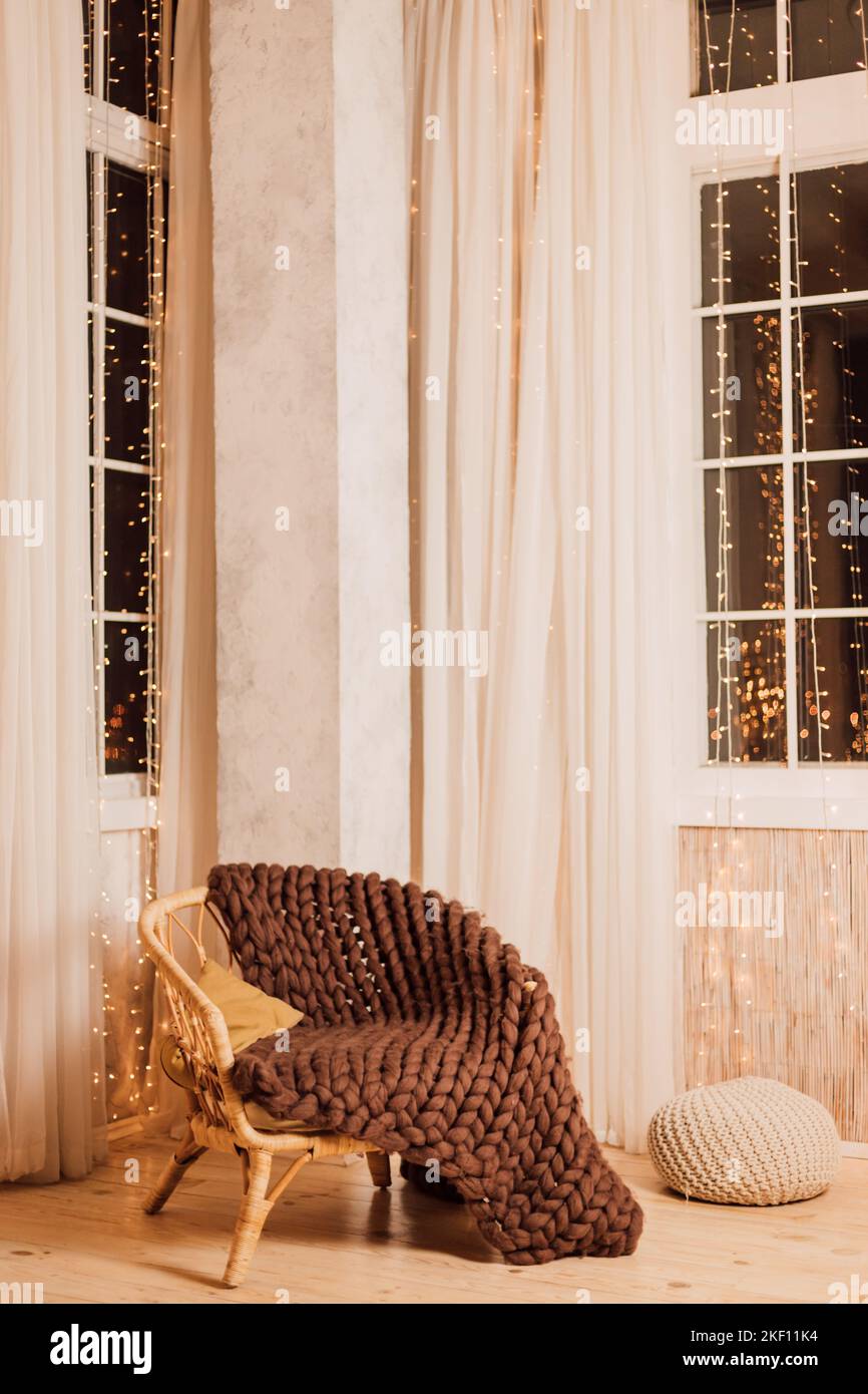 Comoda poltrona moderna con coperta in maglia marrone all'interno vicino alla finestra Foto Stock