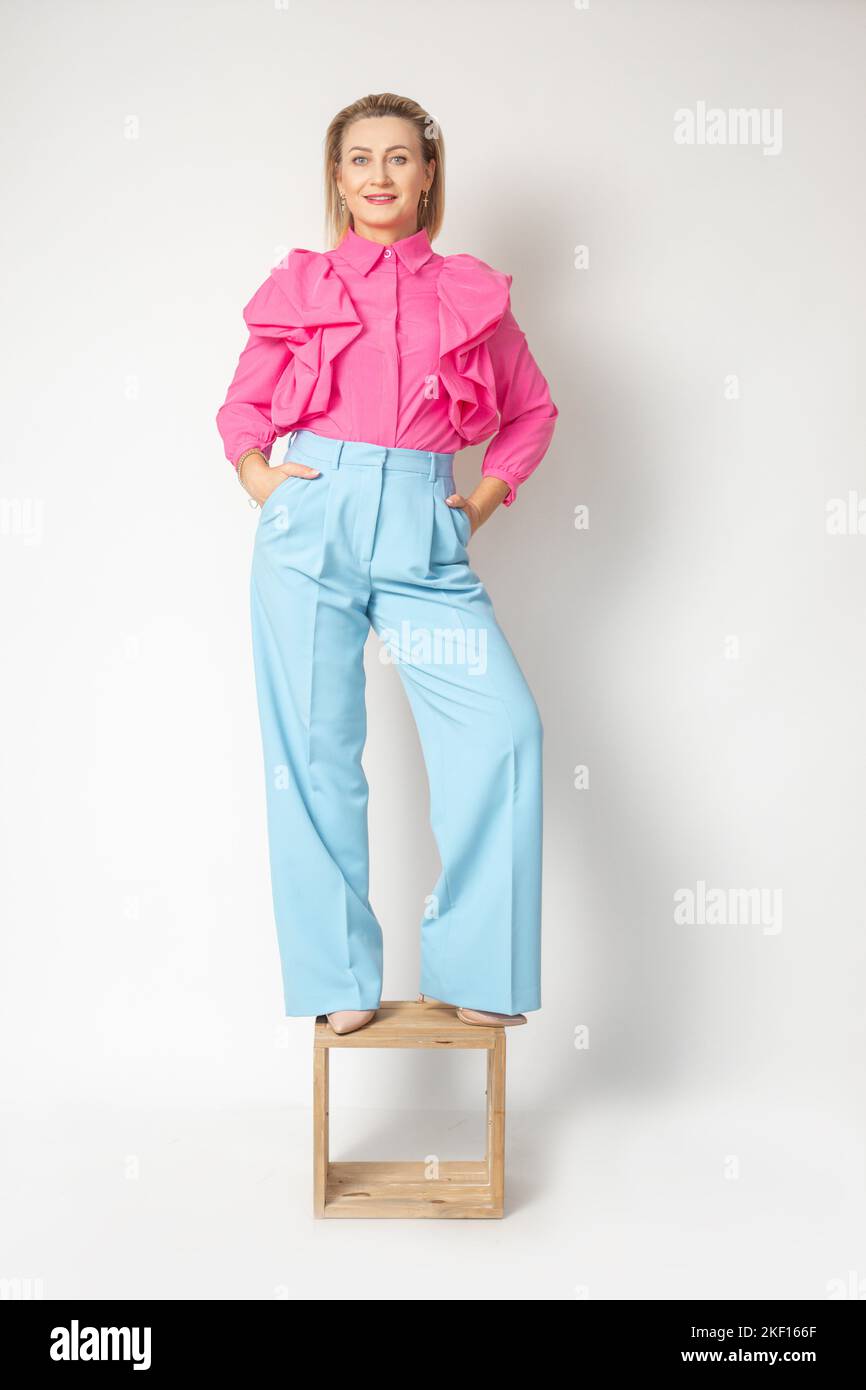 Donna adulta aggraziata in blusa rosa brillante e pantaloni blu in piedi sulla sedia, isolato su bianco. Foto completa di un'azienda sicura e di successo Foto Stock