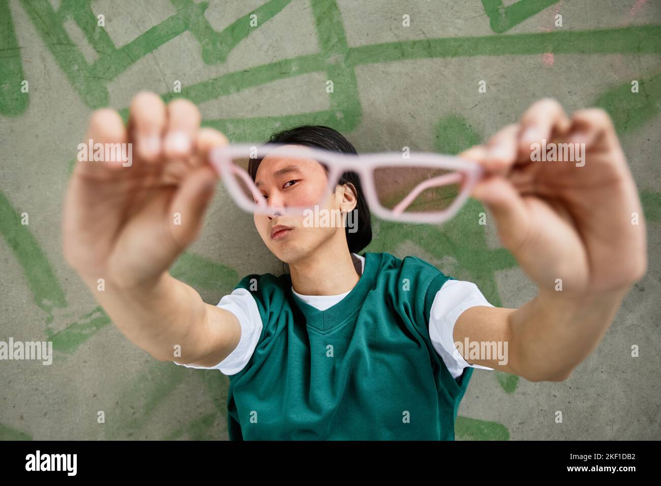 Ritratto di un giovane uomo asiatico che indossa un abbigliamento casual colorato che tiene gli occhiali da sole alla fotocamera Foto Stock