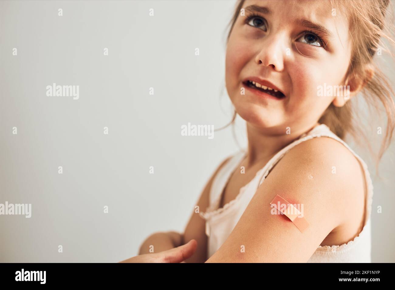 Bambina che sente dolore avendo alcuni effetti collaterali dopo la vaccinazione. Arrossamento, gonfiore, arti doloranti e cefalea come reazione dopo la vaccinazione. Getti Foto Stock