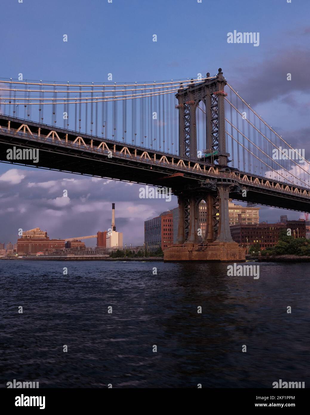 Ripresa ad angolo basso dal fiume East River di Manhattan Bridge contro il cielo nuvoloso del tramonto Foto Stock